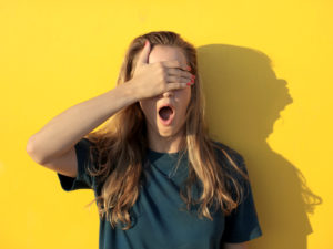 Girl with her mouth open covering her eyes with her hand