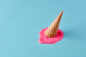 Dropped upside down ice cream cone with melting scoop on pastel blue floor. Minimalistic summer food concept.